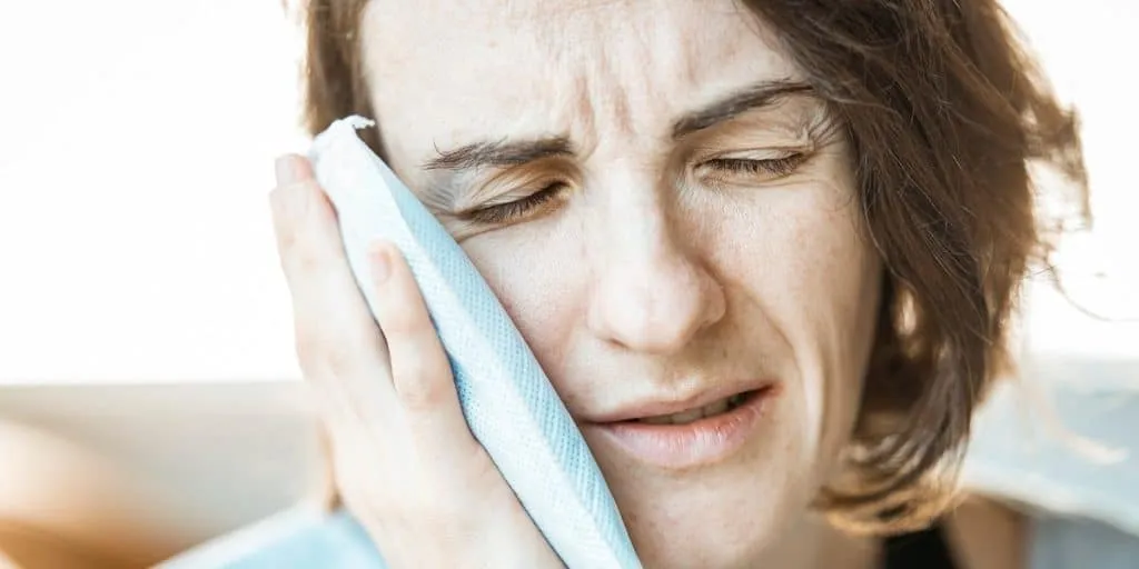 Woman in pain using compress pad on cheek.