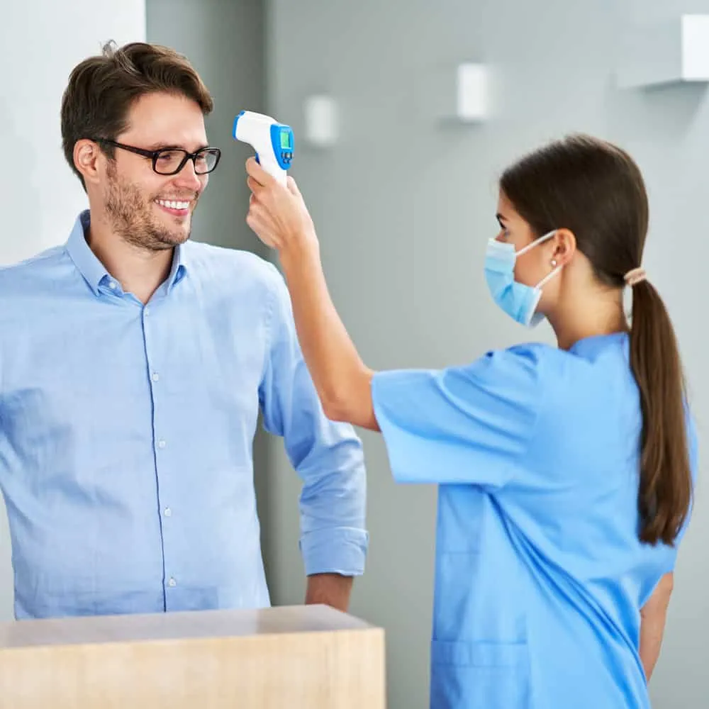 Masked dental staff taking patient's temperature using digital thermometer. Covid-19 protocol.