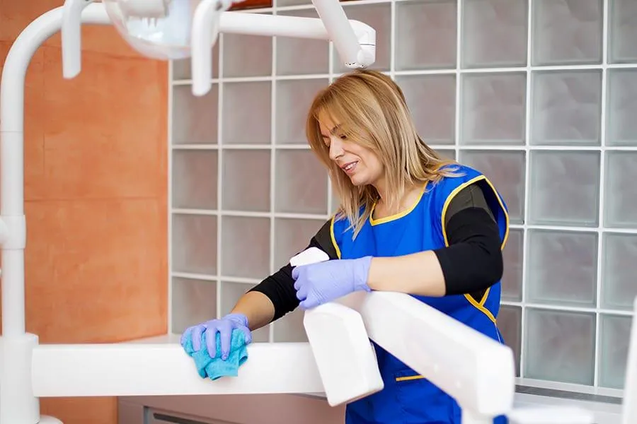 Female dental staff sanitizing dental equipment after Covid-19 protocol.