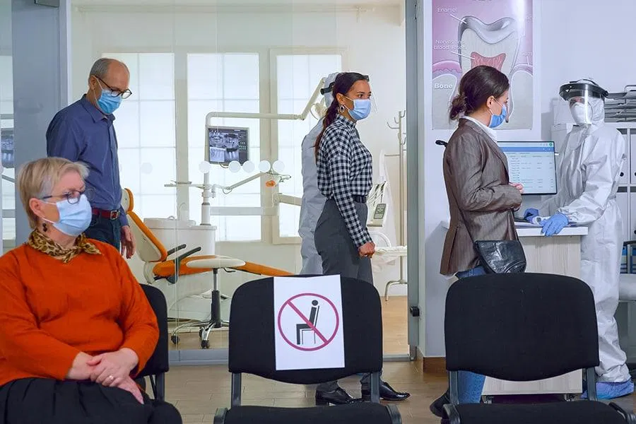 Masked patients in line in the dental office waiting area observing social distancing. Covid-19 protocol.