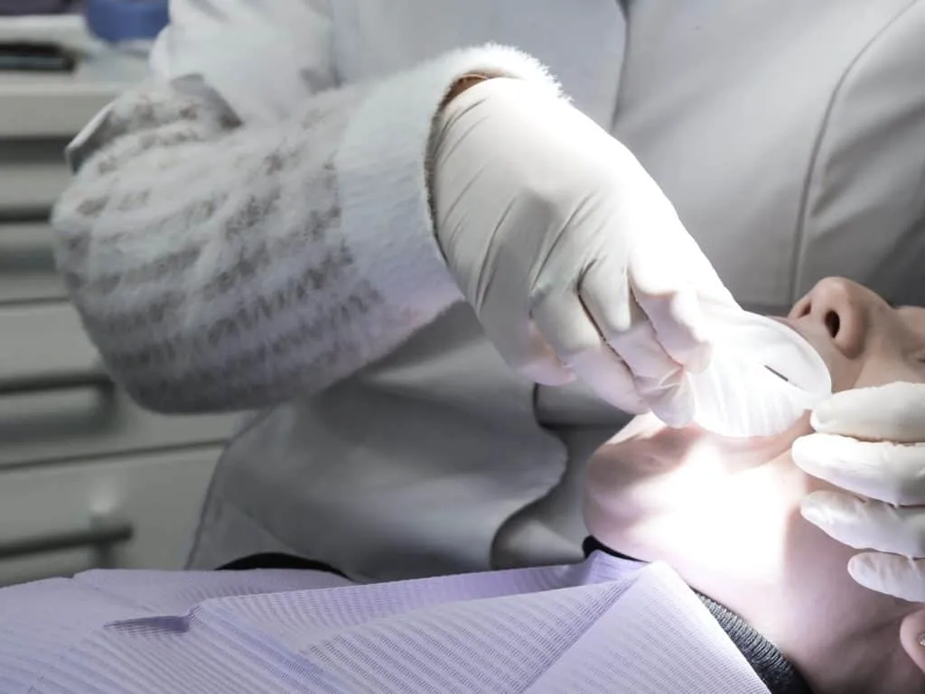 The dentist putting on a rubber dam on the patient's mouth.